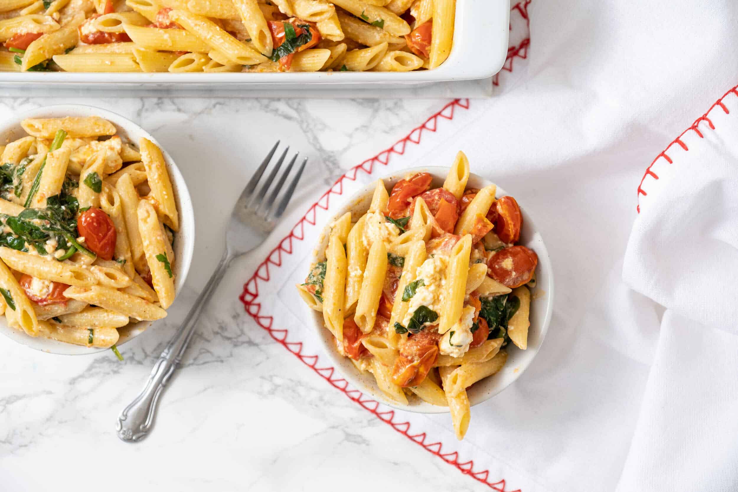 Creamy tomato basil pasta in white bowls with fresh cherry tomatoes and herbs, served on a marble surface with a fork, perfect for easy family dinners.