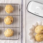 Buttery, freshly baked cookies with chocolate chips and chopped nuts on a cooling rack, with a pat of butter and a white ceramic dish for serving, perfect for homemade cookie recipes.