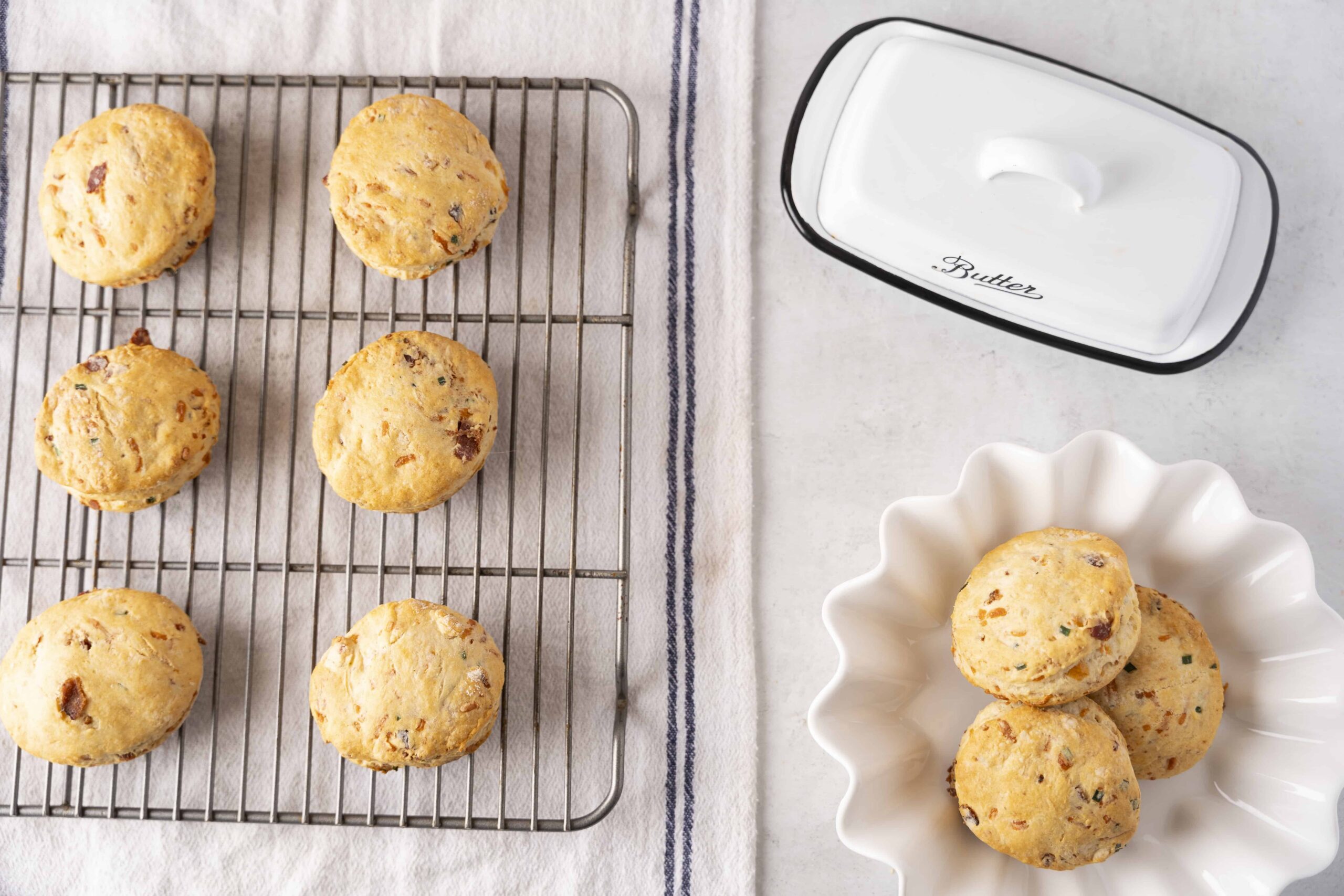 Buttery, freshly baked cookies with chocolate chips and chopped nuts on a cooling rack, with a pat of butter and a white ceramic dish for serving, perfect for homemade cookie recipes.