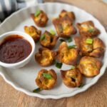 Crispy baked buffalo chicken egg cups garnished with chopped green onions served with a side of spicy buffalo sauce, perfect for a flavorful appetizer or snack.