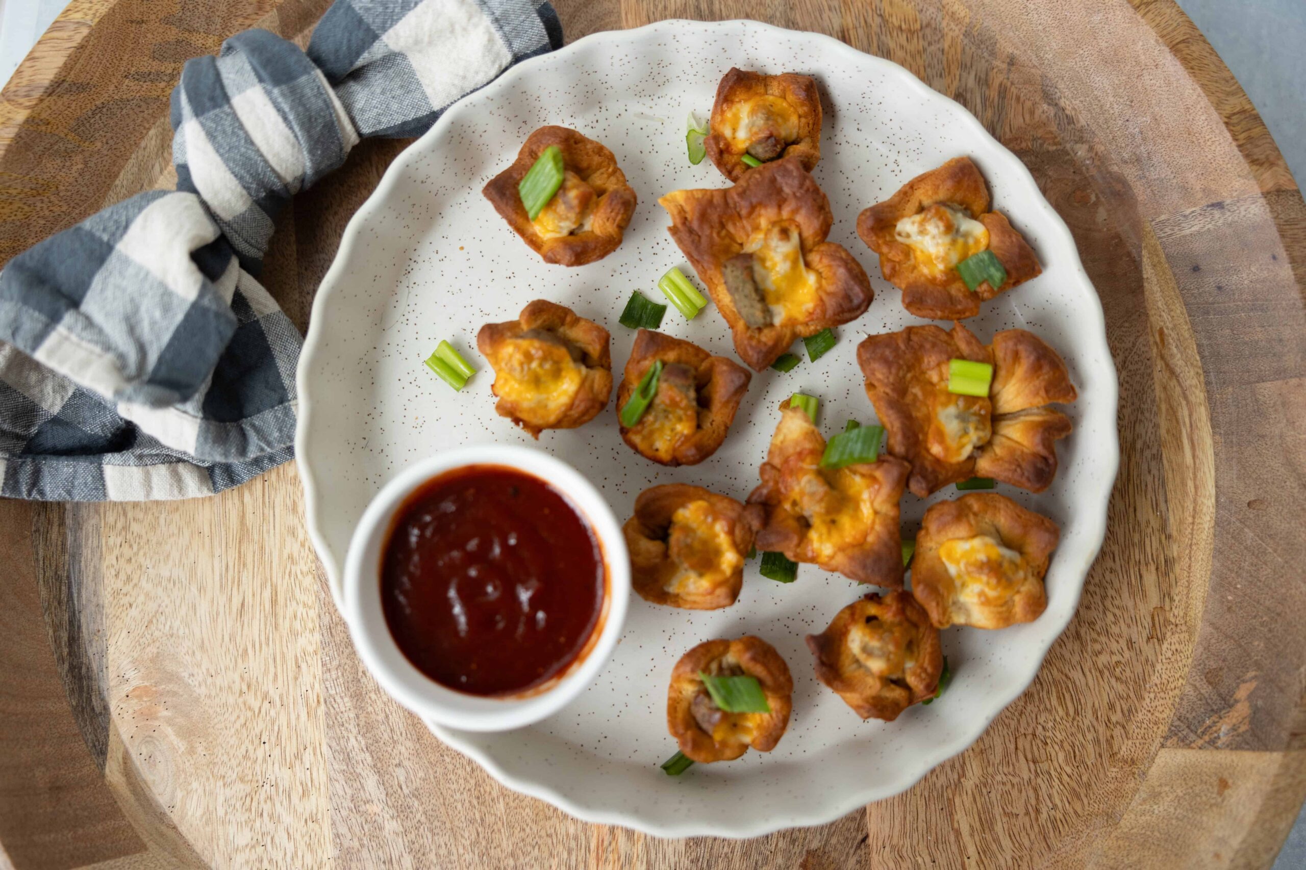 Golden fried wonton appetizers with melted cheese and chopped green onions served with a side of spicy red dipping sauce.