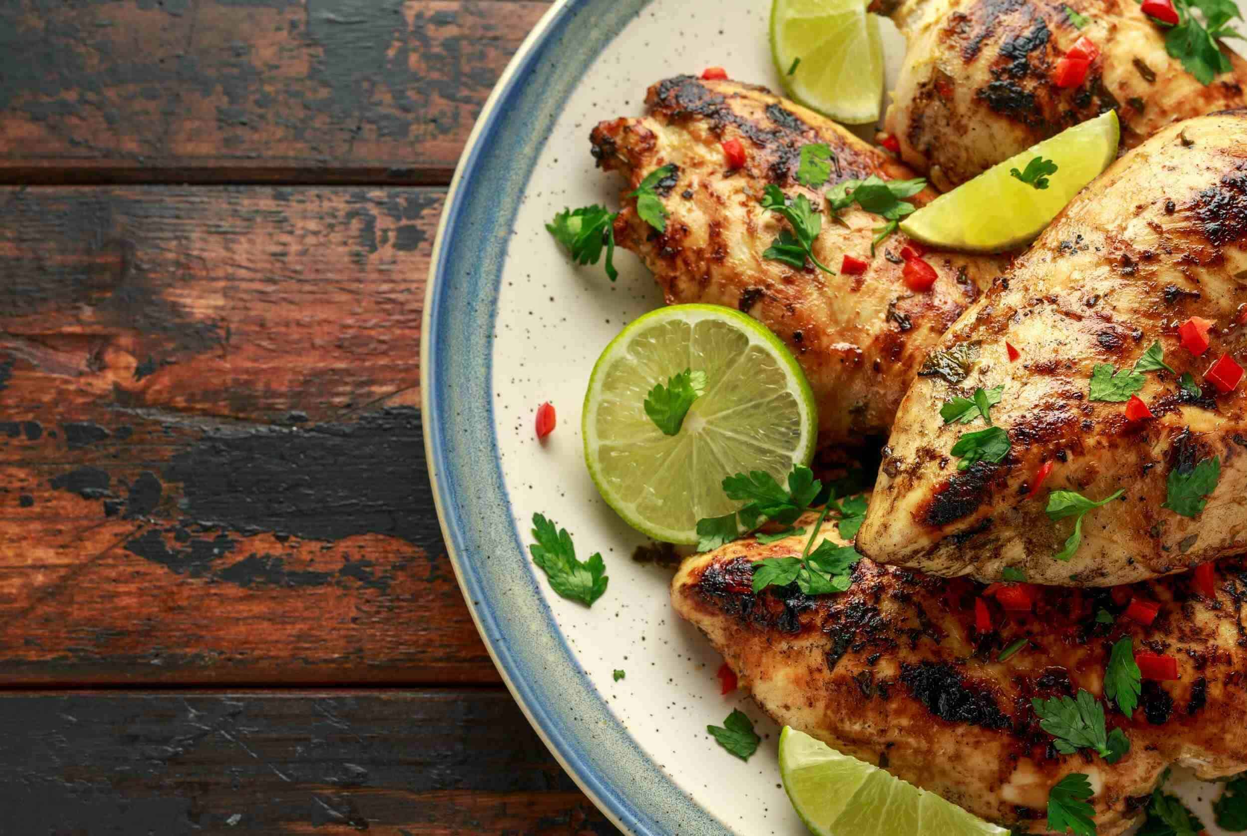 Grilled chicken thighs garnished with fresh cilantro and chopped red peppers, served with lime wedges on a ceramic plate.
