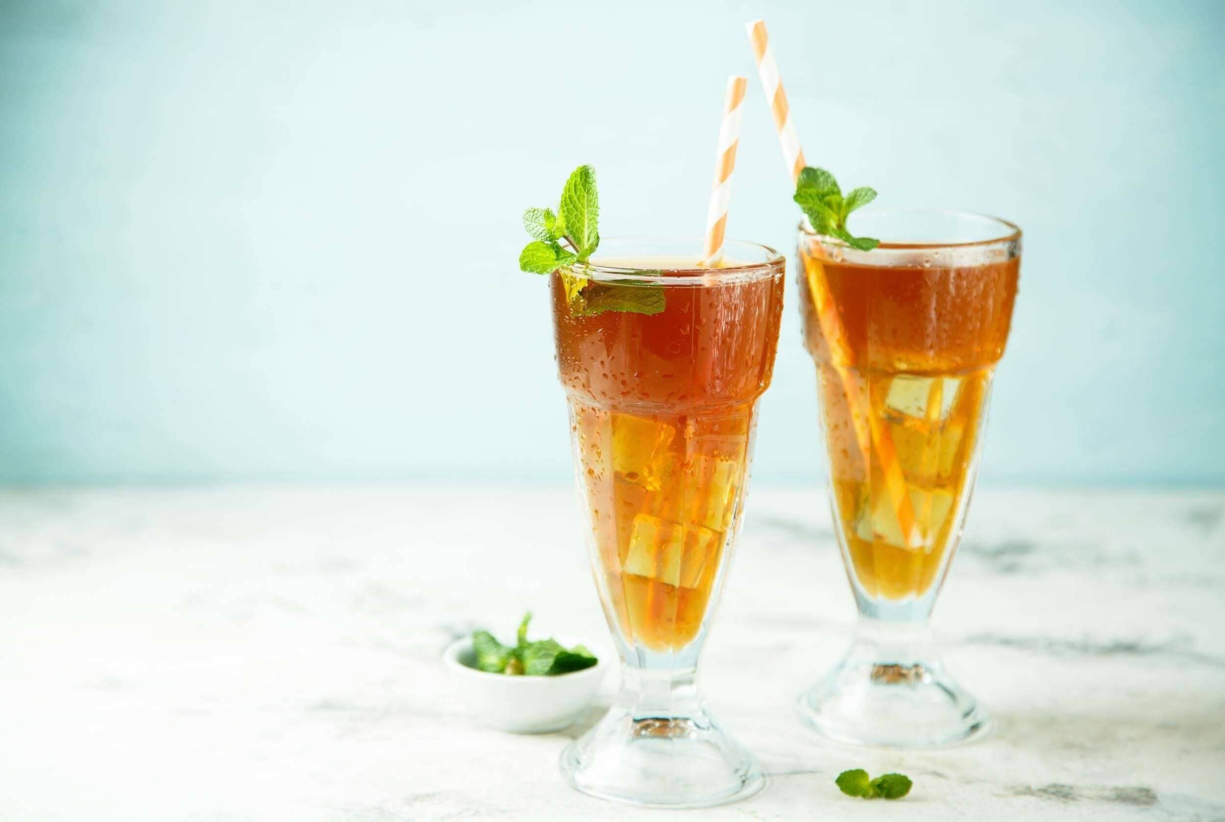 Fresh iced tea with lemon and mint, served in tall glasses with striped straws for a refreshing summer drink. Perfect for hot days or relaxing gatherings.