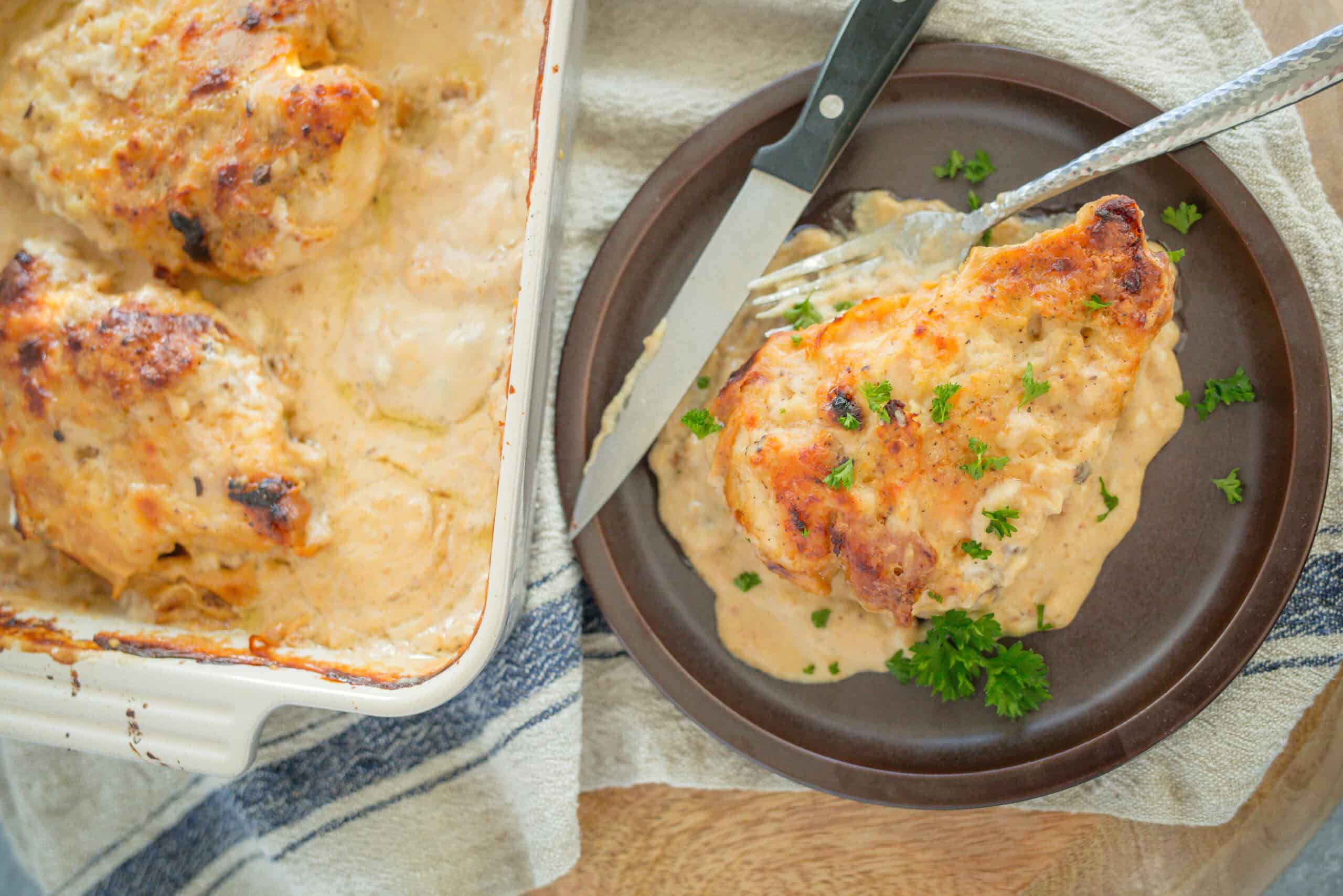 Creamy baked chicken with herb gravy served on a dark plate with fresh parsley garnish. Perfect comfort food for family dinner or special occasion.
