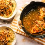 Savory mushroom chicken in garlic sauce served with spaghetti contaminated with a mushroom sauce, garnished with fresh herbs, on a white plate and black skillet.