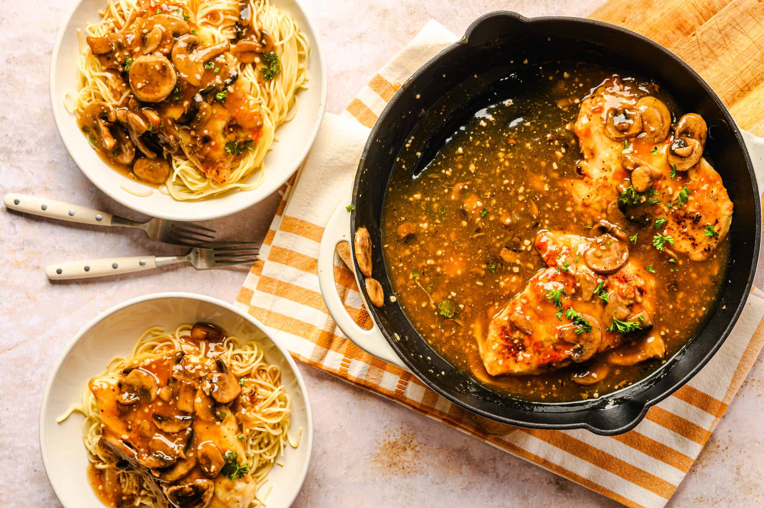 Savory mushroom chicken in garlic sauce served with spaghetti contaminated with a mushroom sauce, garnished with fresh herbs, on a white plate and black skillet.