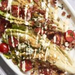 Fresh vegetable wedge salad with cherry tomatoes, bacon, blue cheese, and crispy croutons drizzled with creamy ranch dressing in a white serving dish.