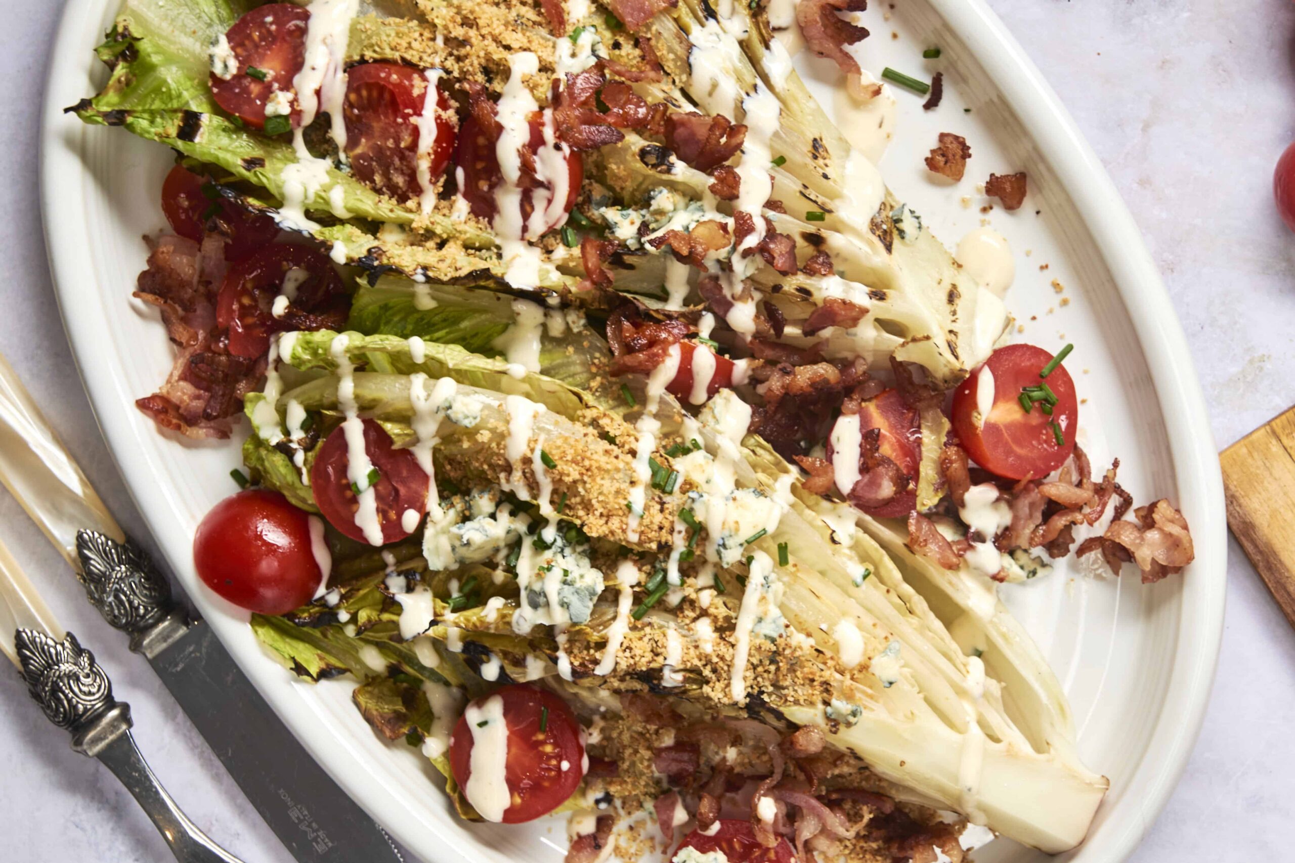 Fresh vegetable wedge salad with cherry tomatoes, bacon, blue cheese, and crispy croutons drizzled with creamy ranch dressing in a white serving dish.