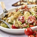 Golden-brown vegetable and cheese casserole on white dish with cherry tomatoes and fresh herbs, served with a fork, vibrant and appetizing, perfect comfort food.
