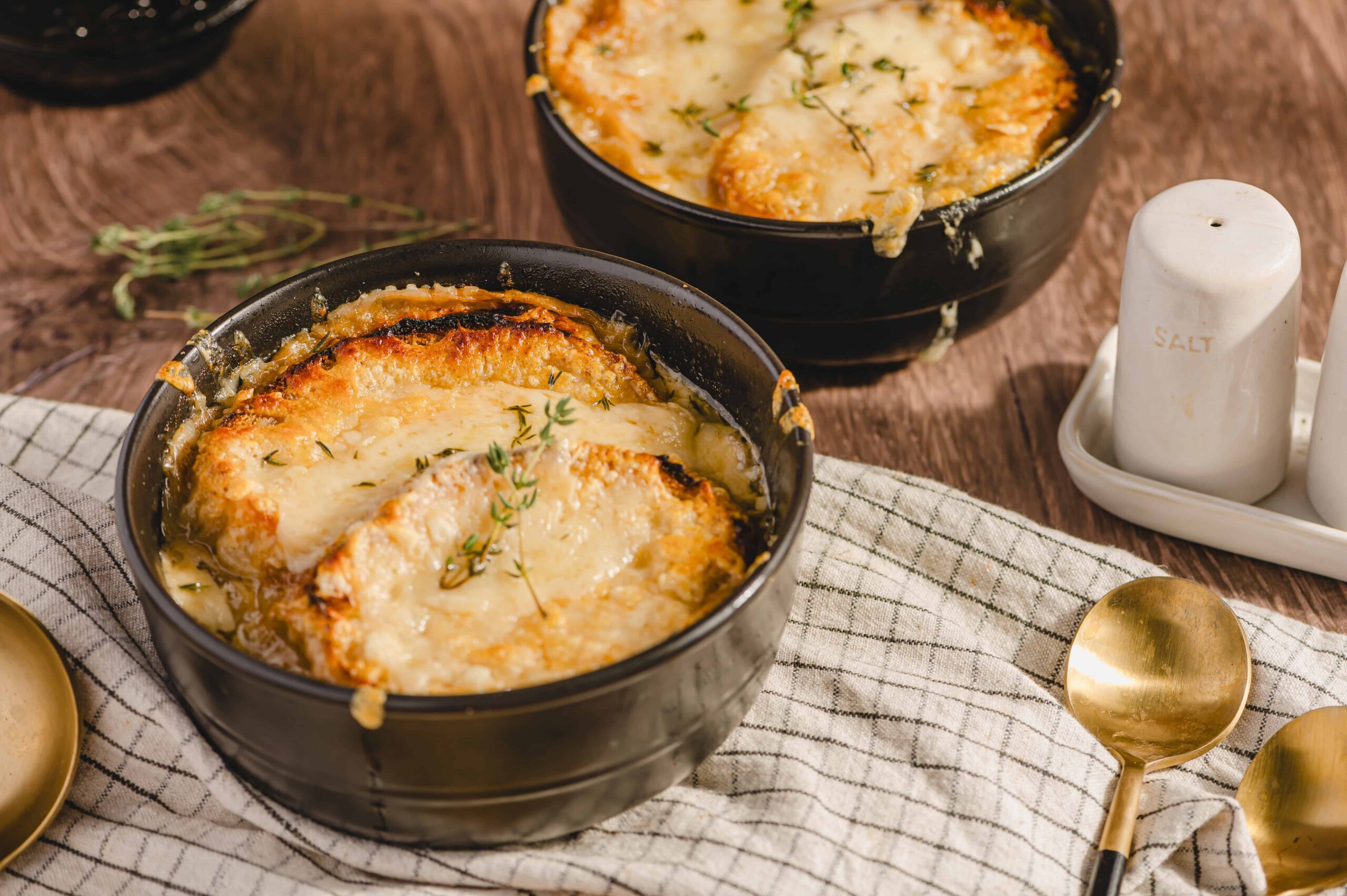 Golden baked French onion soup in black bowls garnished with thyme on a rustic wooden table.