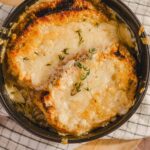 Creamy baked cauliflower gratin with melted cheese and fresh thyme in a black baking dish, served on a rustic checkered cloth.