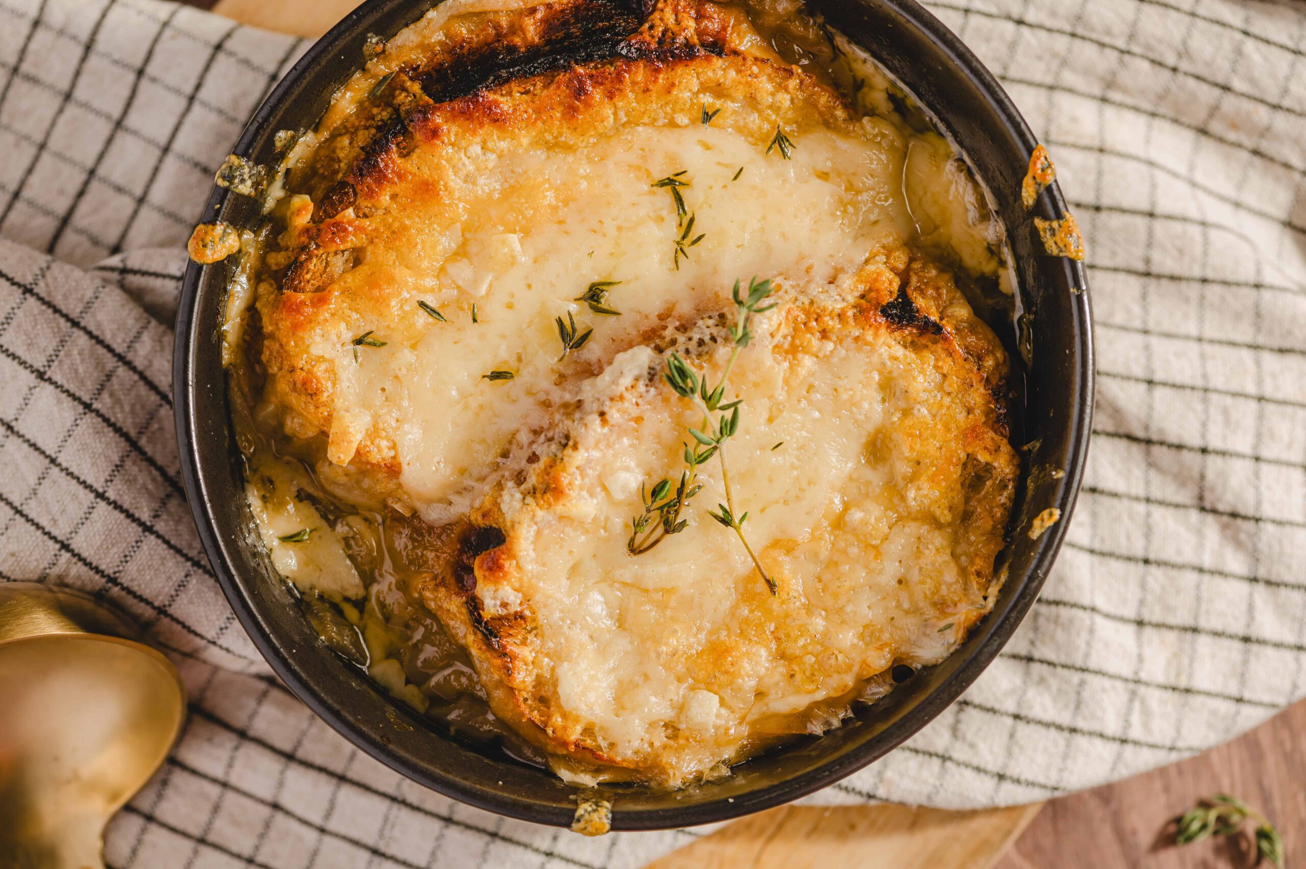 Creamy baked cauliflower gratin with melted cheese and fresh thyme in a black baking dish, served on a rustic checkered cloth.