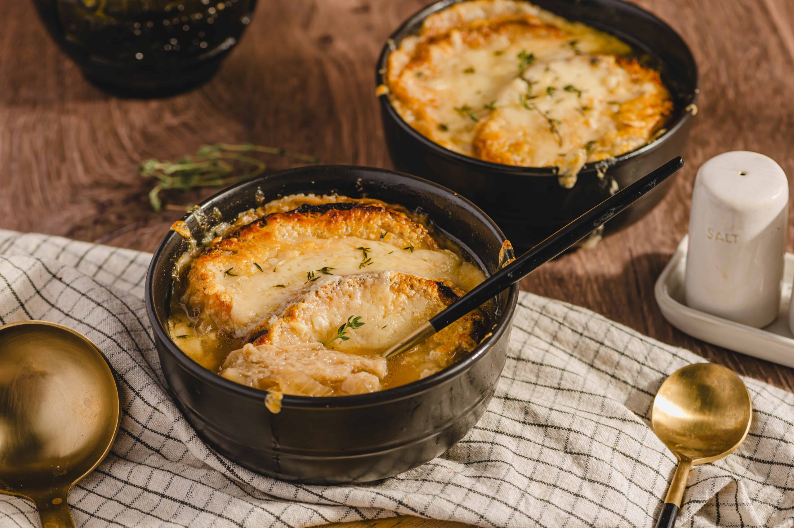 Creamy chicken pot pie dessert with melted cheese in black bowls on rustic wooden table with gold spoons and salt shaker.