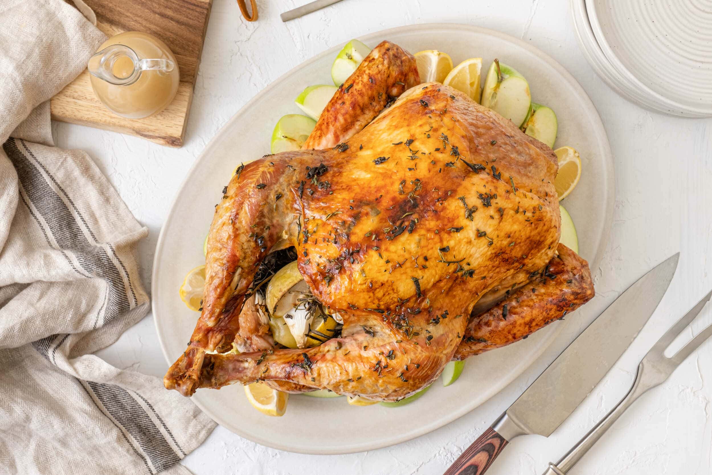 Juicy roasted whole chicken garnished with herbs on a white serving platter with lemon and apple slices for a wholesome family meal.