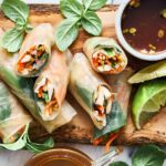 Fresh Vietnamese spring rolls filled with colorful vegetables and herbs, served with lime wedges and dipping sauce on a rustic wooden platter. Perfect for healthy, vegan, or gluten-free meals.