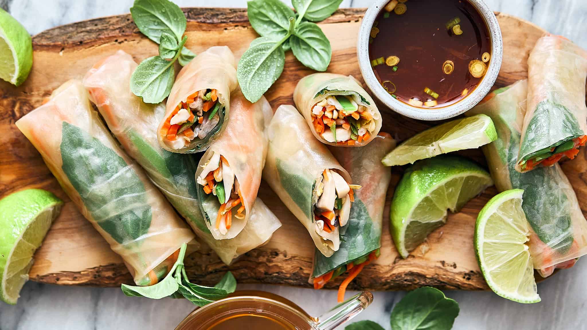 Fresh Vietnamese spring rolls filled with colorful vegetables and herbs, served with lime wedges and dipping sauce on a rustic wooden platter. Perfect for healthy, vegan, or gluten-free meals.
