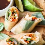 Fresh Vietnamese spring rolls filled with shredded vegetables and herbs, served with dipping sauces on a rustic wooden board. Perfect for healthy, light appetizers or snacks.