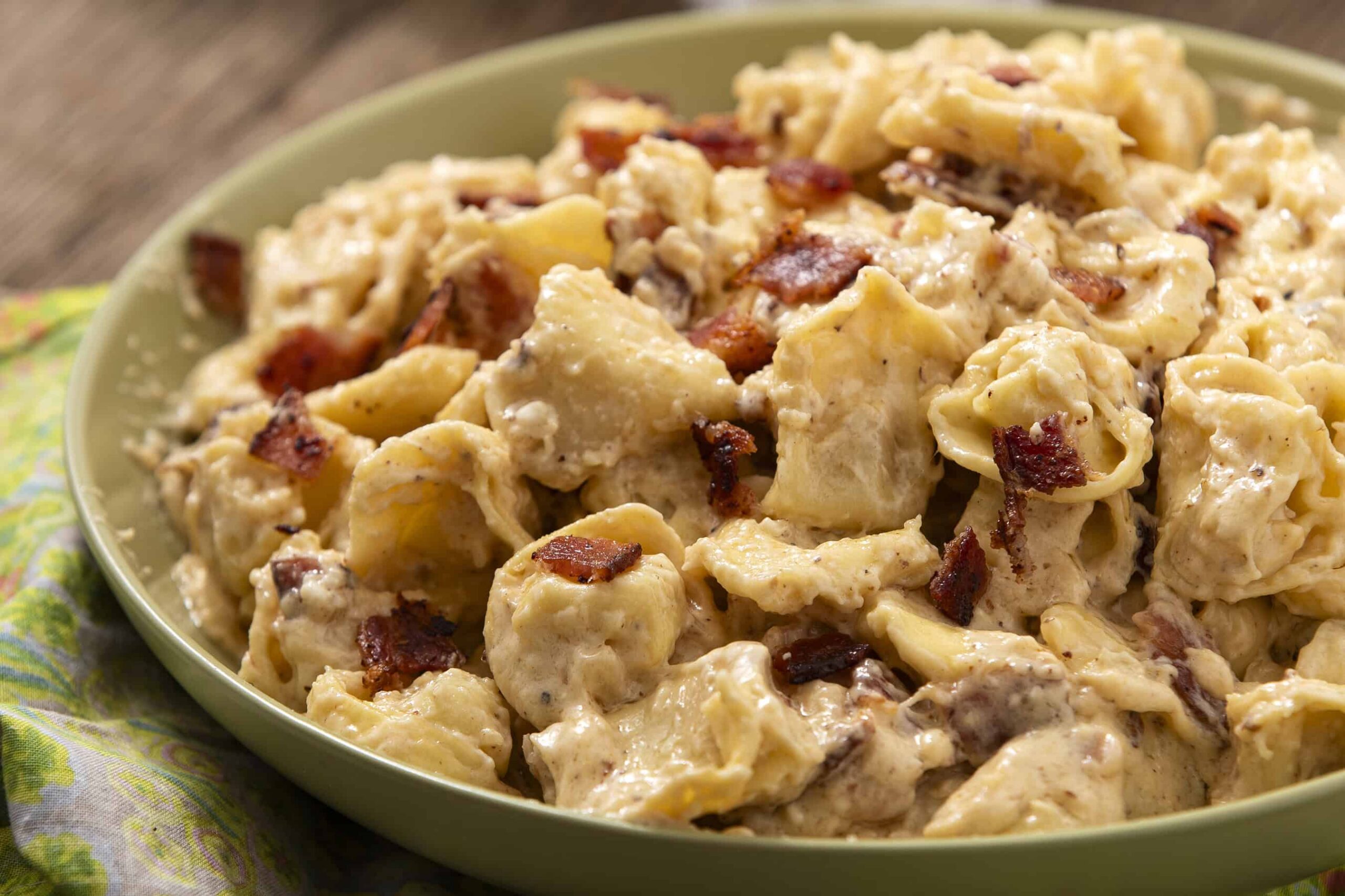 Creamy chicken and bacon pasta dish served in a green bowl, topped with crispy bacon bits, featuring tender chicken chunks and a rich sauce, perfect for comfort food recipes.