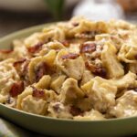 Savory creamy chicken and bacon pasta in a green bowl, topped with crispy bacon bits, served on a colorful cloth. Perfect comfort food for a hearty meal.