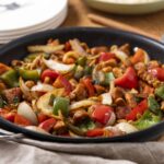 Stir-fried chicken with colorful bell peppers and onions in a black skillet, showcasing a vibrant, healthy, and flavorful Asian-inspired dish.
