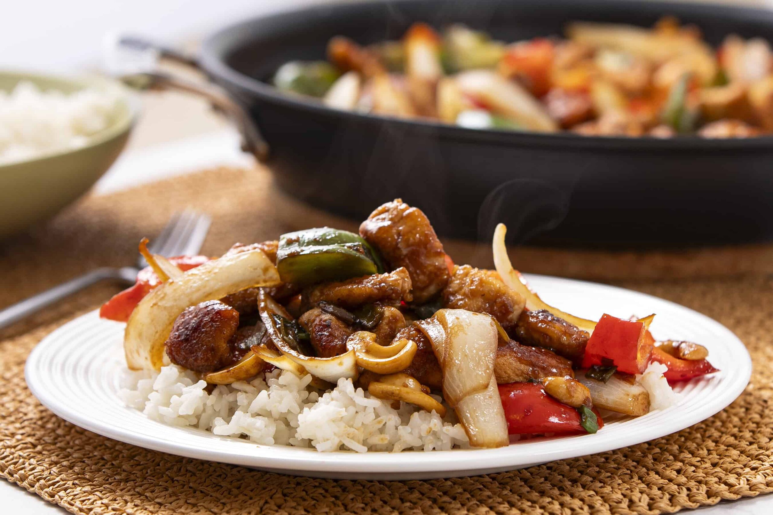 Steamed rice topped with savory stir-fried vegetables and tender pieces of meat, served on a white plate with a flavorful sauce and colorful peppers, showcasing an Asian-inspired dish.