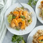 Juicy shrimp and lime on a bed of seasoned rice served on white plates, garnished with fresh cilantro and lime wedges; delicious seafood dish perfect for quick, easy meals.