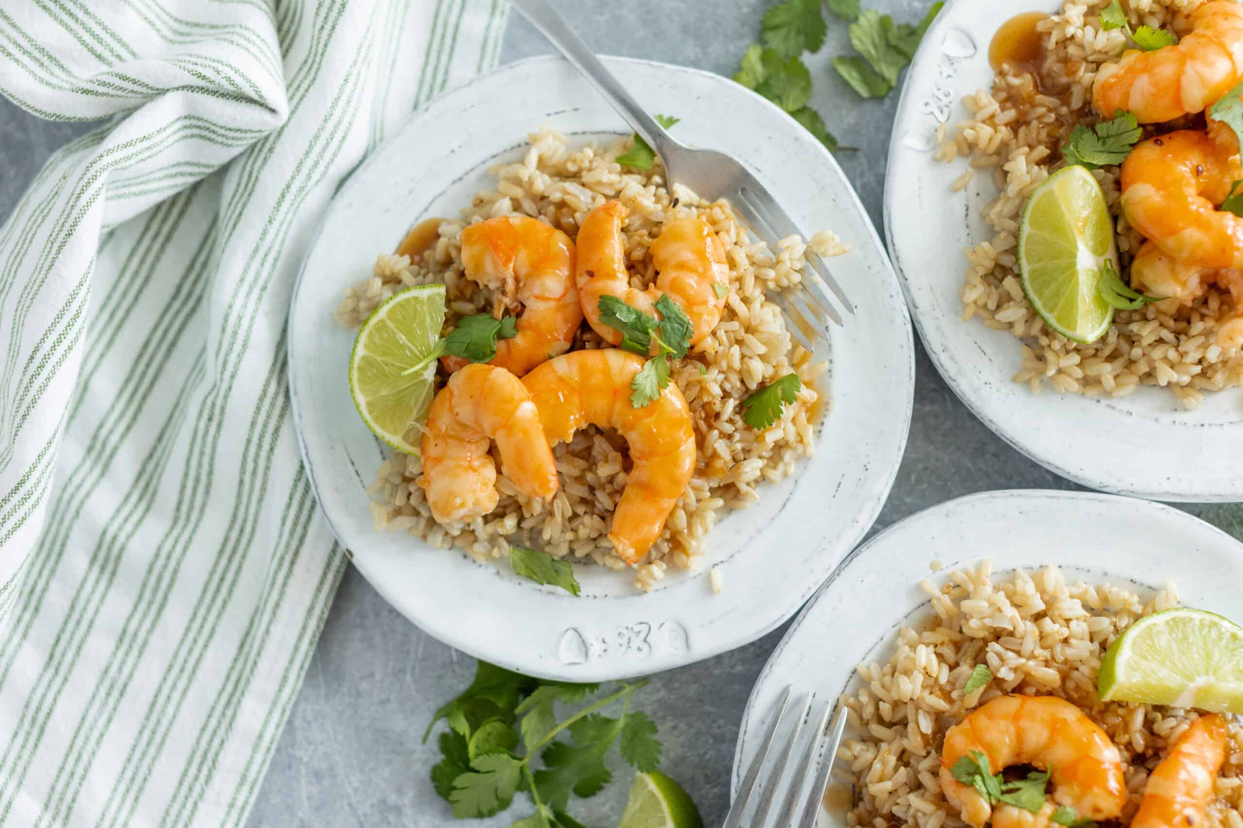 Juicy shrimp and lime on a bed of seasoned rice served on white plates, garnished with fresh cilantro and lime wedges; delicious seafood dish perfect for quick, easy meals.