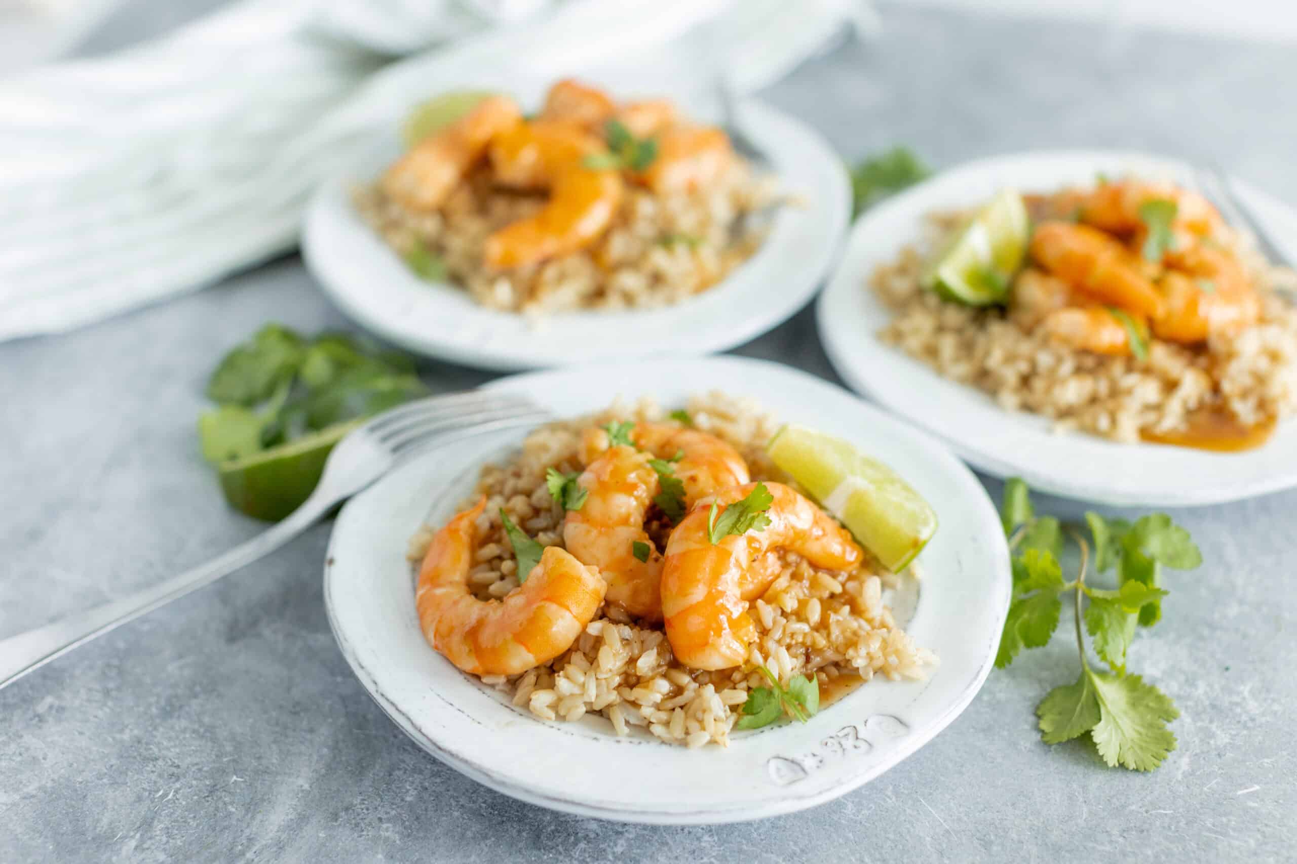 Fresh shrimp taco rice bowls on white plates with lime wedges and cilantro, served with flavorful rice, garnished with herbs, perfect for Mexican-inspired dinner or lunch, vibrant food presentation.