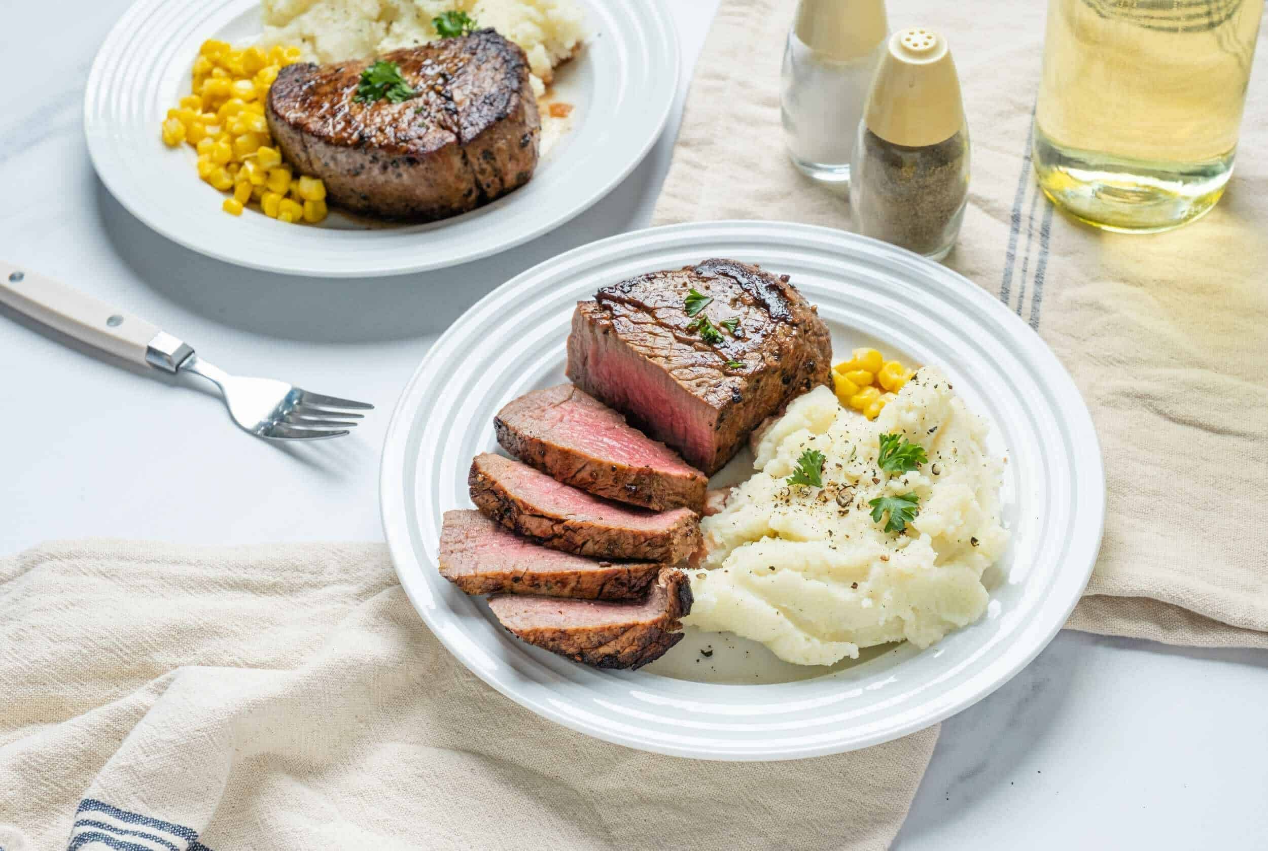 Juicy cooked steak with mashed potatoes and corn on a white plate, perfectly prepared beef dinner, delicious and tender meat served with classic mashed potatoes and seasonal corn.