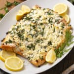 Delicious baked salmon topped with crumbled feta cheese, fresh herbs, and lemon wedges on a white platter. Perfect for a healthy seafood dinner or lunch.