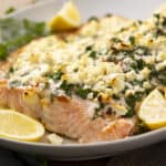Juicy baked salmon fillet topped with crumbled feta cheese, fresh herbs, and lemon slices on a white platter, perfect for healthy seafood recipes and dinner ideas.