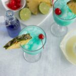 Refreshing blue tropical drinks garnished with pineapple slices and maraschino cherries, served with lime wedges, perfect for summer parties.