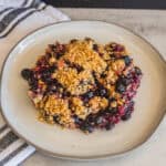 Fresh berry crumble topped with golden, crunchy streusel served on a white ceramic plate, perfect for dessert or sweet snack.