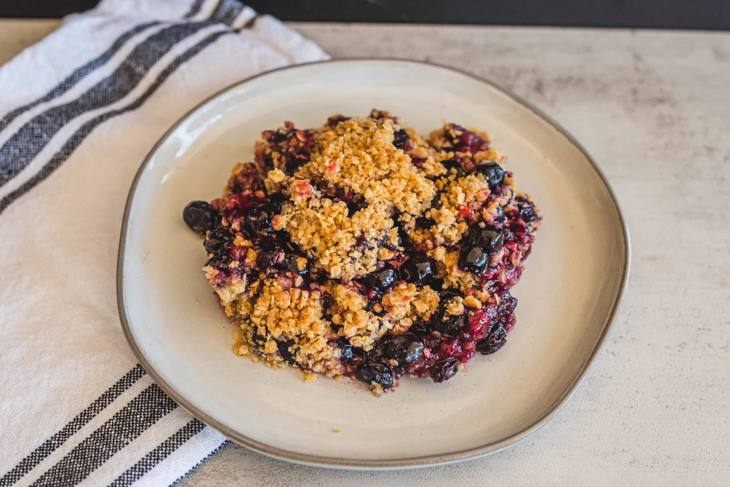 Fresh berry crumble topped with golden, crunchy streusel served on a white ceramic plate, perfect for dessert or sweet snack.