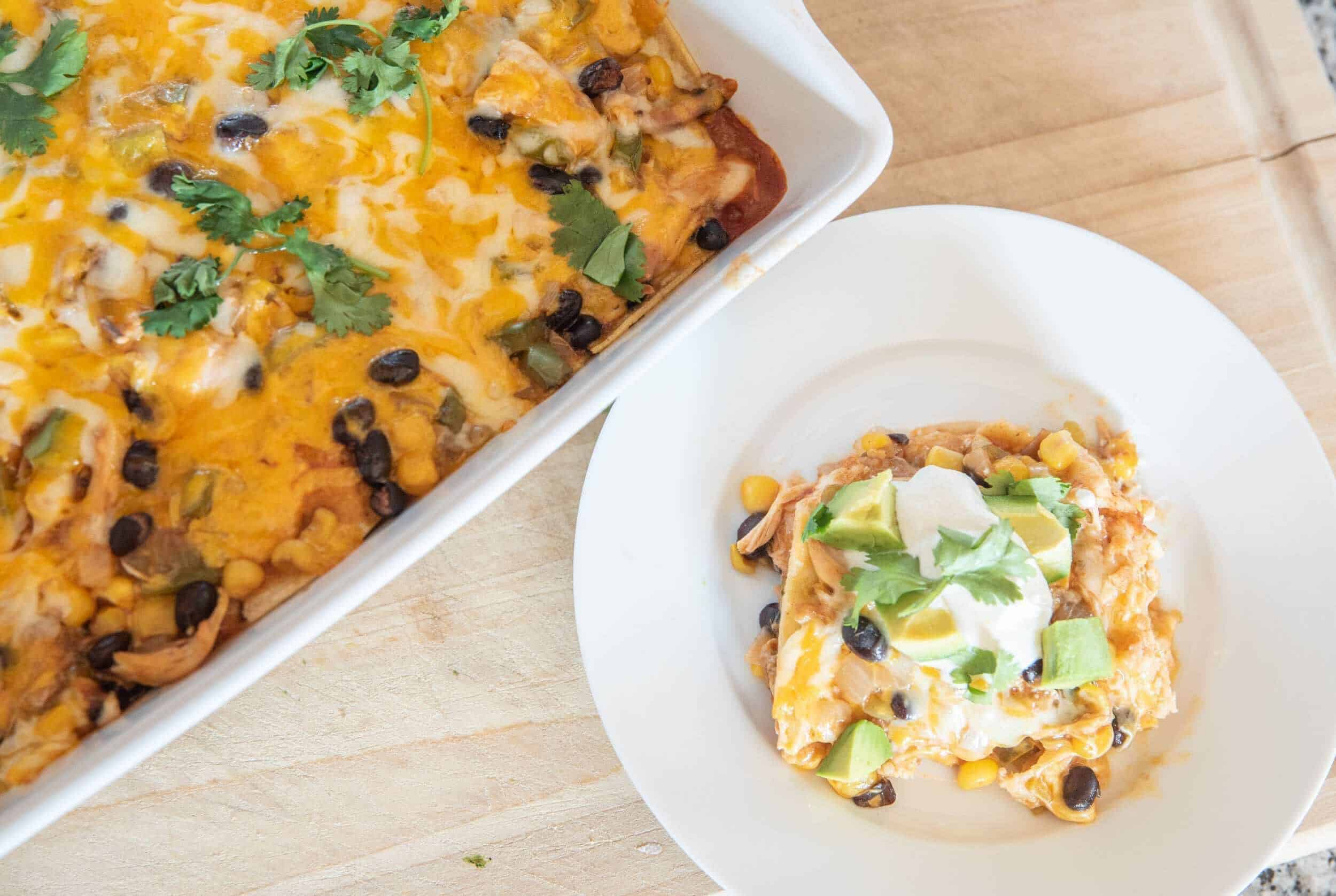 Cheesy chicken enchiladas with black beans, corn, and avocado served with fresh cilantro on top.