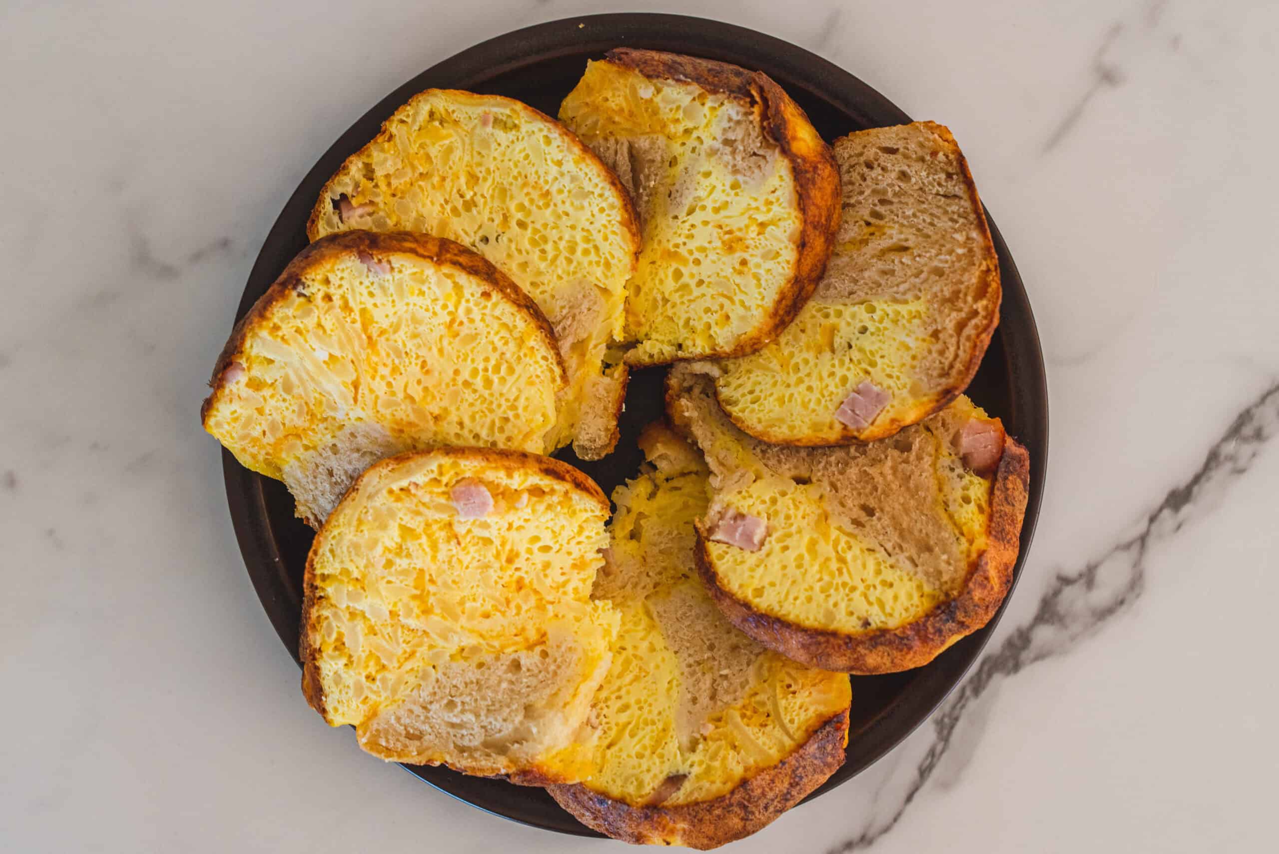 Fluffy, golden baked egg muffins with ham in a black dish, served as a delicious breakfast or brunch option. Perfectly cooked with a light, airy texture, ideal for meal prep or weekend mornings.
