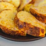 Crispy baked potato slices with melted cheese and ham on a black plate, close-up, comforting potato dish, delicious cheesy potato bake, easy recipe for baked potatoes.