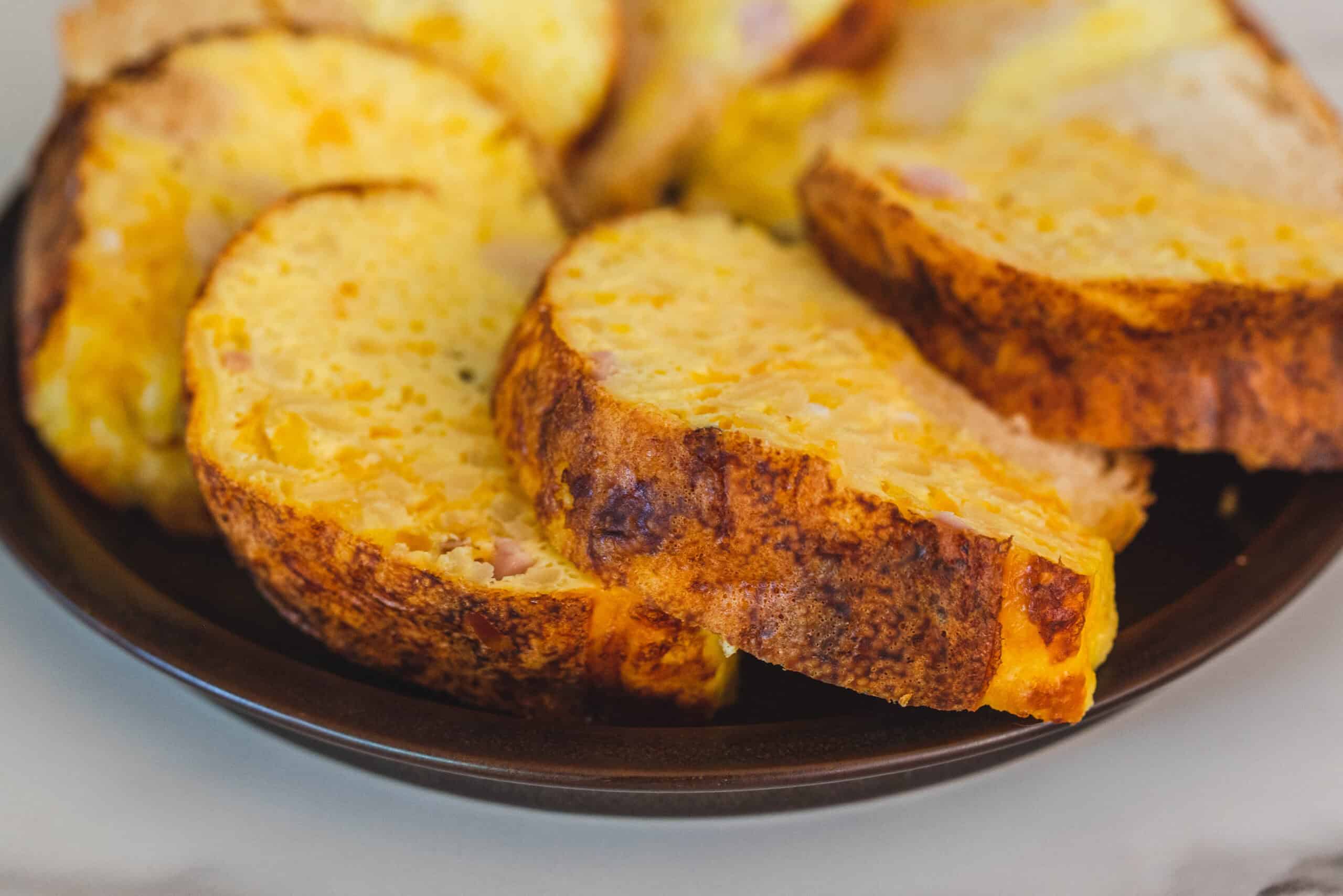 Crispy baked potato slices with melted cheese and ham on a black plate, close-up, comforting potato dish, delicious cheesy potato bake, easy recipe for baked potatoes.