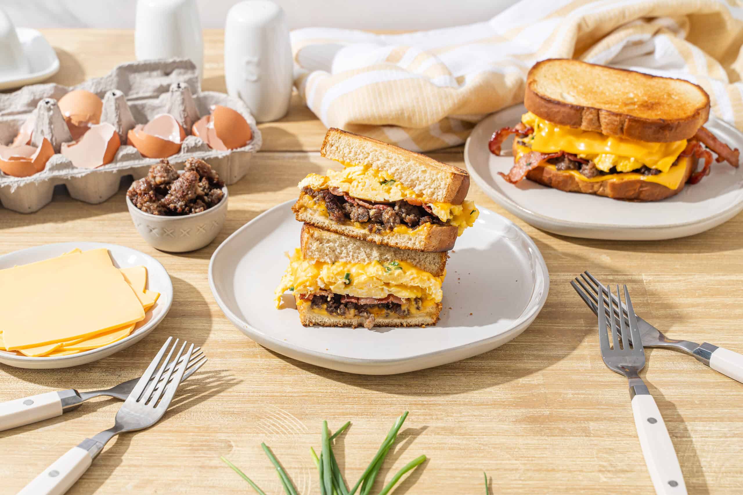 Savory breakfast sandwich with scrambled eggs, cooked bacon, sausage, and cheese on toasted bread, served with breakfast ingredients like cheese, eggs, and sausage links.
