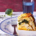 Broccoli and cheese stuffed chicken pot pie with golden crust on a white plate with blue floral design, served with a fork and a glass of water.