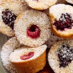 Delicious mini berry sponge cakes with fresh raspberries and blackberries, dusted with powdered sugar on a white plate. Perfect for dessert or tea time treats.