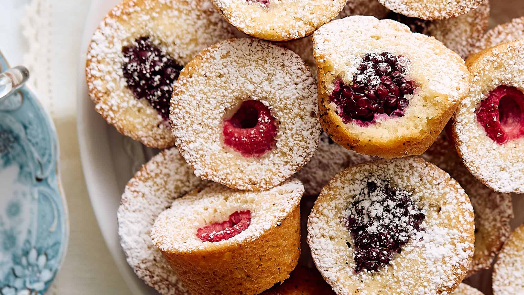 Delicious mini berry sponge cakes with fresh raspberries and blackberries, dusted with powdered sugar on a white plate. Perfect for dessert or tea time treats.