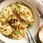 Creamy onion and garlic pasta with grated Parmesan cheese on top, served on a rustic ceramic plate. Fresh herbs garnish this delicious Italian-inspired dish, perfect for a comforting meal.