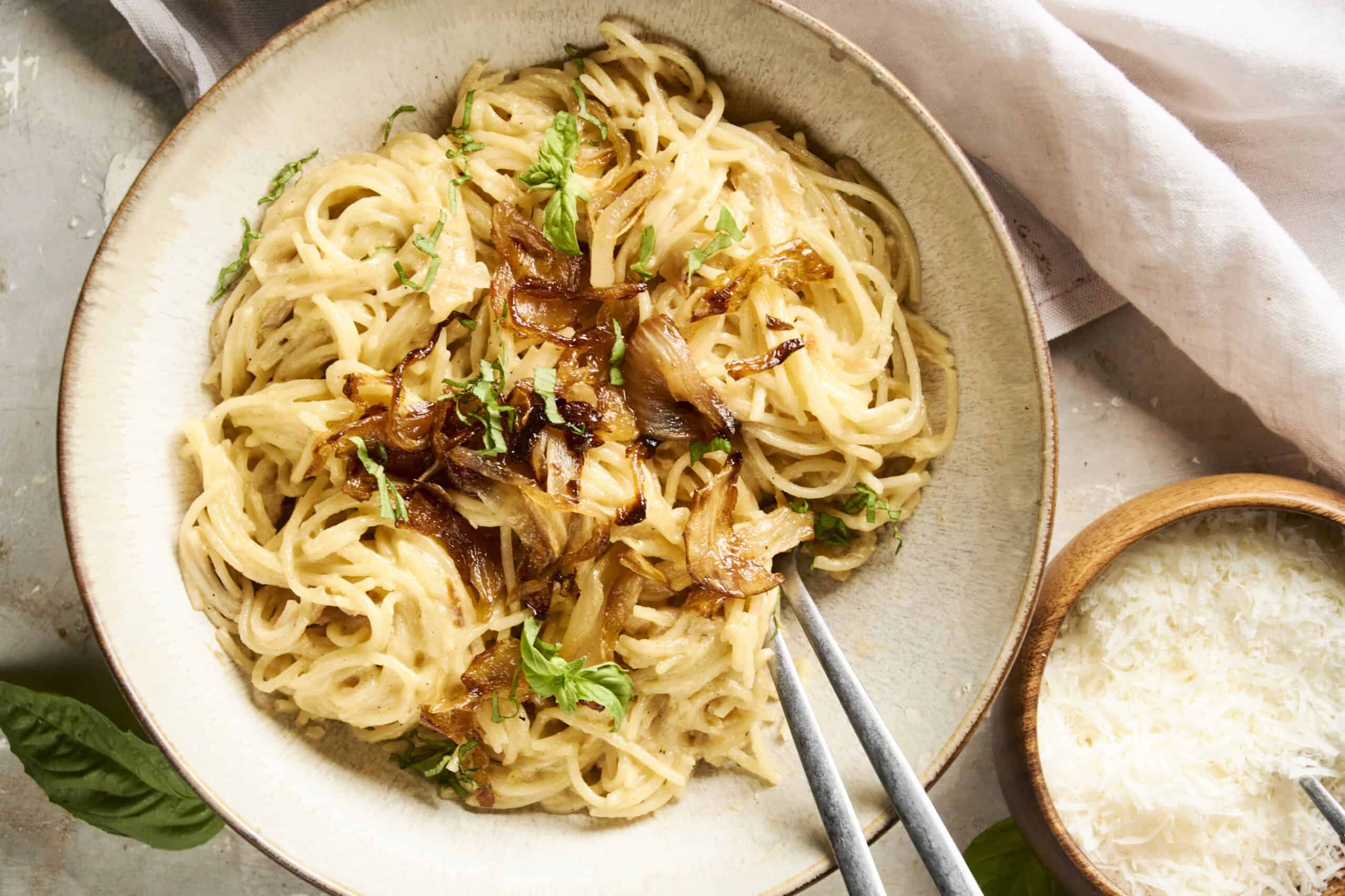 Creamy onion and garlic pasta with grated Parmesan cheese on top, served on a rustic ceramic plate. Fresh herbs garnish this delicious Italian-inspired dish, perfect for a comforting meal.