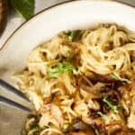 Creamy mushroom Alfredo pasta served on a rustic ceramic plate with chopped herbs and caramelized onions, paired with a bowl of fluffy white rice for a delicious Italian-inspired meal.