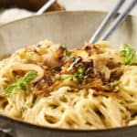 Creamy chicken alfredo pasta dish garnished with fresh basil, served in a rustic bowl with crispy bacon bits and garlic slices for a flavorful Italian-inspired meal.
