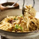 Creamy mushroom pasta with herbs in a rustic bowl, fork lifting a portion, served with crispy bacon bits and fresh basil garnish, perfect comfort food.