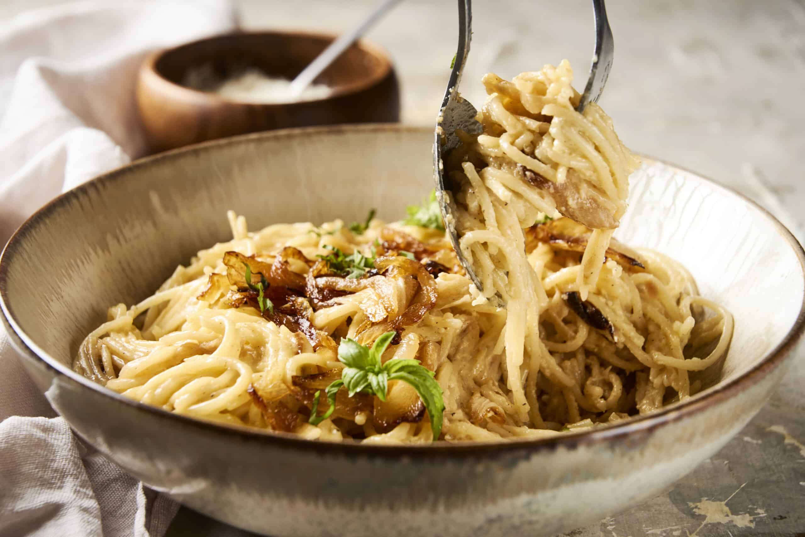 Creamy mushroom pasta with herbs in a rustic bowl, fork lifting a portion, served with crispy bacon bits and fresh basil garnish, perfect comfort food.