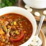 Hearty homemade vegetable and ground meat soup served in a white bowl with fresh herbs, perfect for cozy meals and cold weather; garnished with chopped greens.