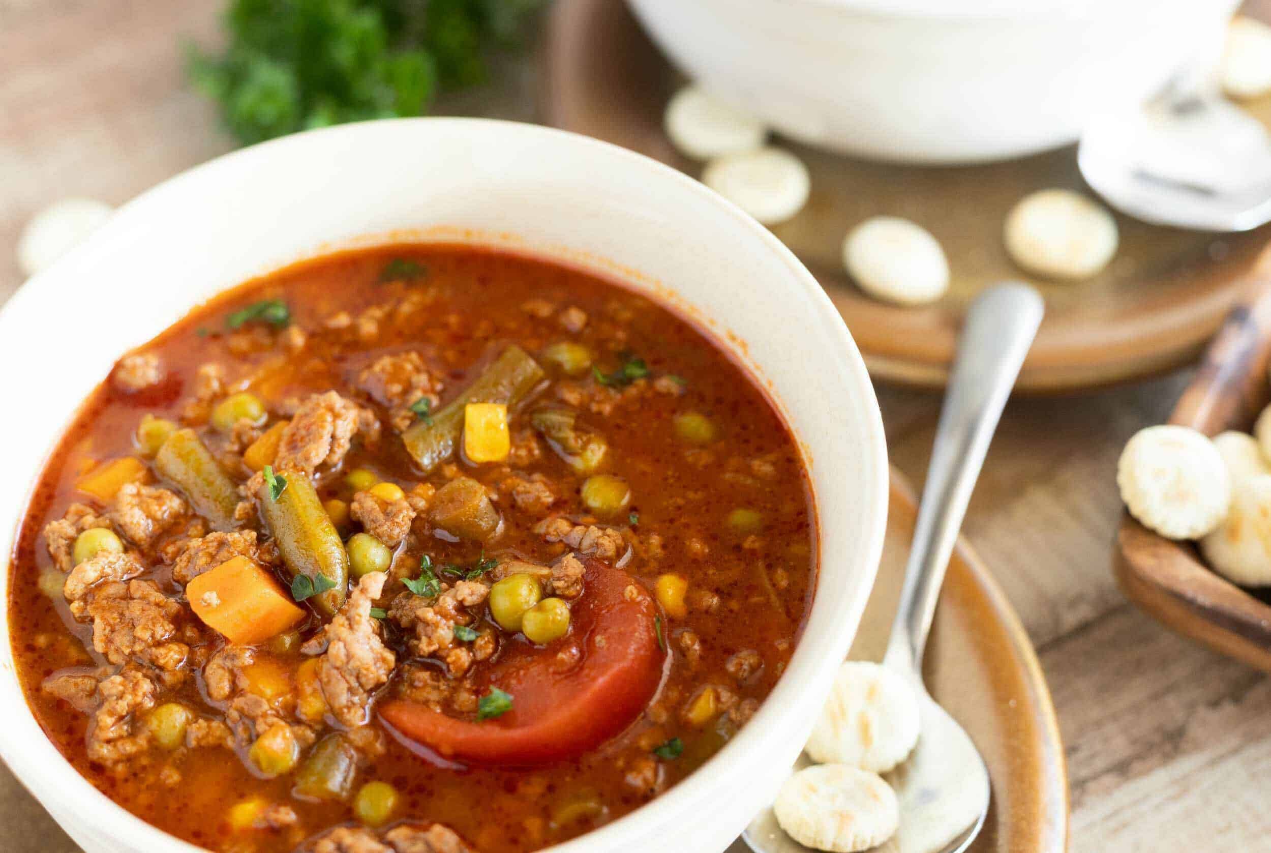 Hearty homemade vegetable and ground meat soup served in a white bowl with fresh herbs, perfect for cozy meals and cold weather; garnished with chopped greens.